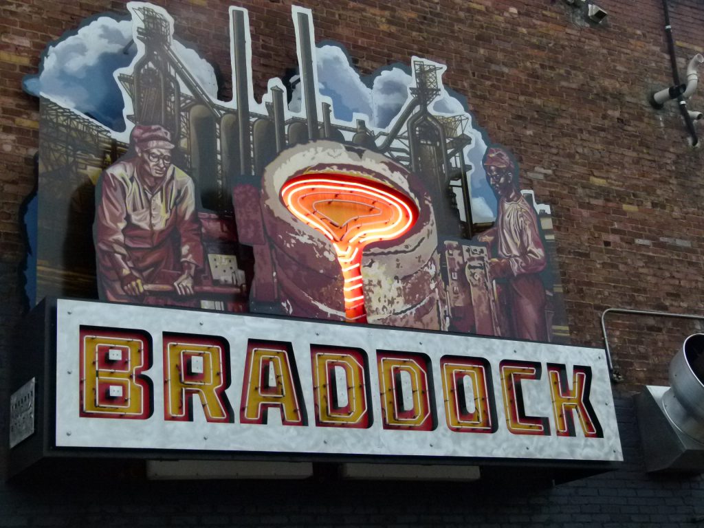 A neon sign highlighting Braddock's steel making history on the side of Superior Motors.