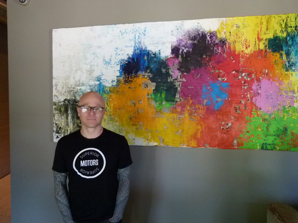 Chef/owner Kevin Sousa at the host station of Superior Motors in front of a painting by Pittsburgh artist Mia Tarducci.