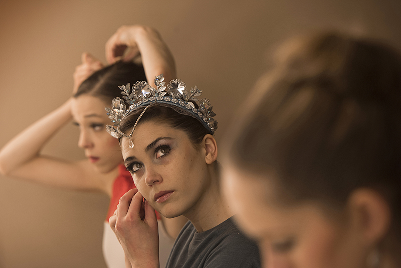 Corps dancer Caitlin Peabody puts on earrings as she prepares for her role as Snow Queen backstage with other leading ladies.