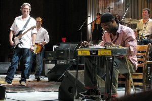 Robert Randolph playing the pedal steel guitar while Eric Clapton looks on. Photo: Steve Proctor via Wikimedia Commons lic.