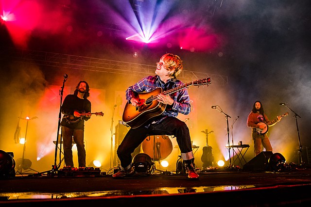 Billy Strings playing acoustic guitar strings in a 2021 concert. (Photo: Taylor-Sandal and Wikipedia)