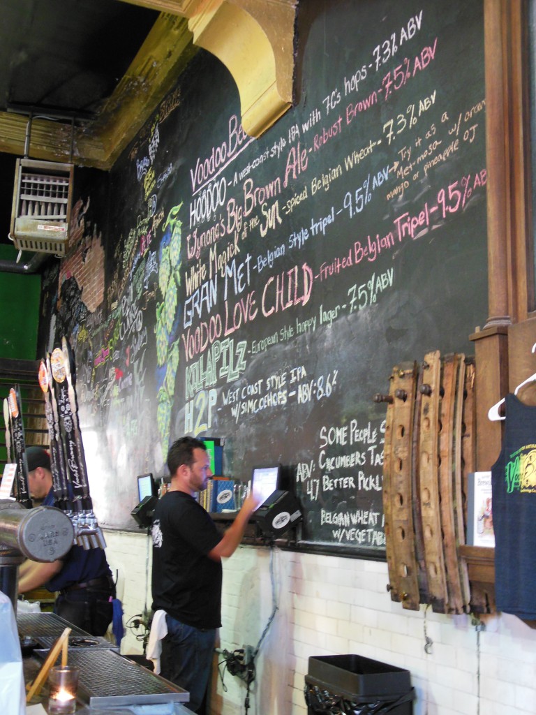 A bartender cashes out a patron beneath the colorful, chalked draft list. Beyond are the names of volunteers who helped get Voodoo Homestead off the ground.