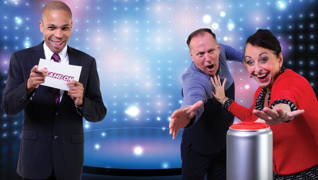 Game show contestants (Tim Brady and Christine Laitta) reach for the big red button as the 'Game On' host (Jason Shavers) runs the contest. (Photo: Archie Carpenter).