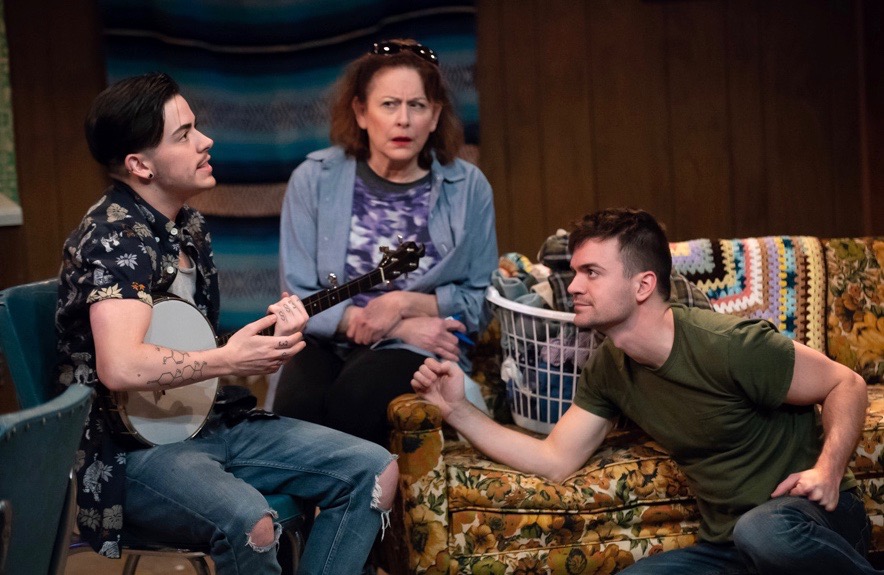 There’s nothing like banjo music to bring a fractured family together—especially banjo music from a trans teen! Max (Liam Ezra Dickinson, L) gamely gives Mom’s latest scheme a try.