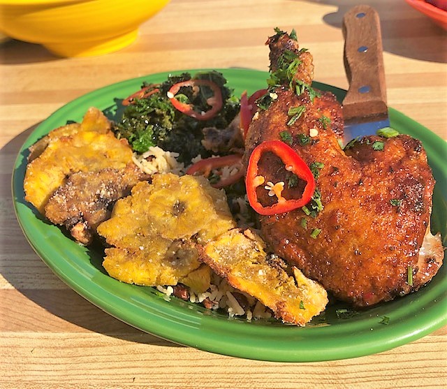Cilantro flakes and red pepper slices adorn the jerk chicken, with sides of greens, rice, and tostones.