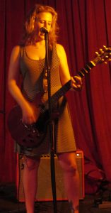 Tammy plays a powerful downstroke chord on her guitar while singing.